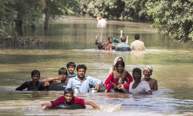 Flood victims wade through a flooded area along a road as they wait for help, in Multan, Punjab province